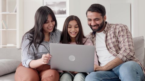 Happy family portrait. Parents with child daughter watching funny videos using laptop computer having fun enjoying spending leisure time together at home in living room sitting on sofa.