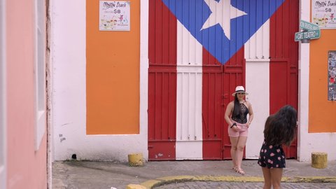 Old San Juan Puerto Rico 02-20-2021 Two girls talking photos in front of Puerto flag door