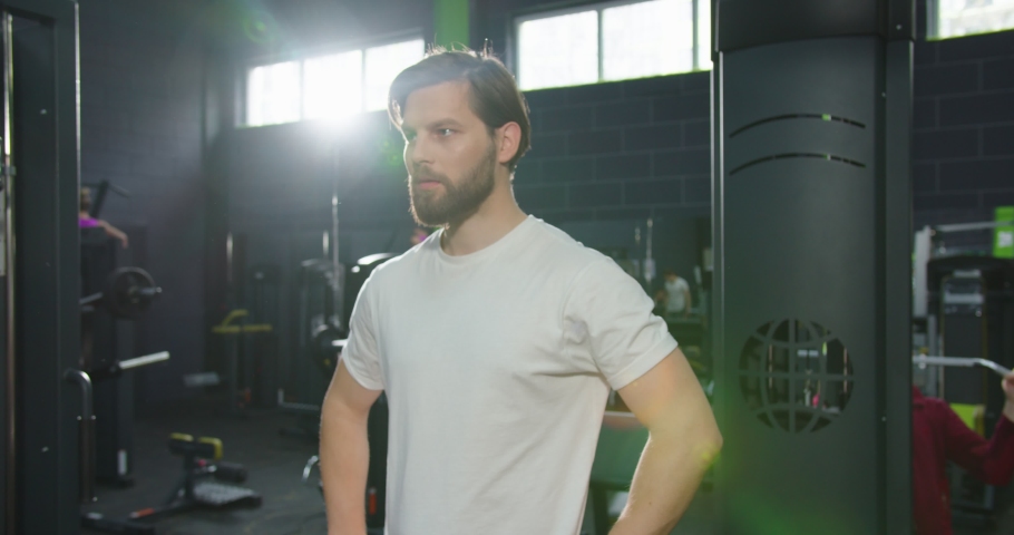 Portrait view of the bearded confident coach or trainer standing arms crossed at the gym and looking confidently at the camera after training. Sport and recreation concept