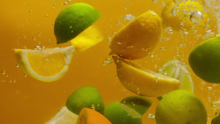 Close-up of falling sliced limes, oranges and lemons into the water on orange background, making a cocktail of citrus fruits, drinking cold lemonade, shooting of carbonated water with sliced fruits.  | Shutterstock HD Video #1073399885