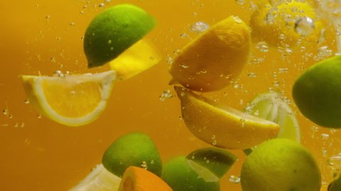Close-up of falling sliced limes, oranges and lemons into the water on orange background, making a cocktail of citrus fruits, drinking cold lemonade, shooting of carbonated water with sliced fruits. 