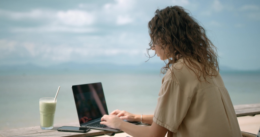 Women seat at the beach bar and works freelance, she having matcha late drink