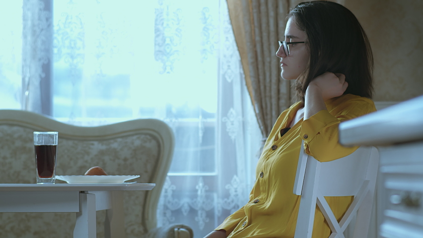 A brunette girl in glasses sits at a table and drinks a drink from a glass, quenches her thirst