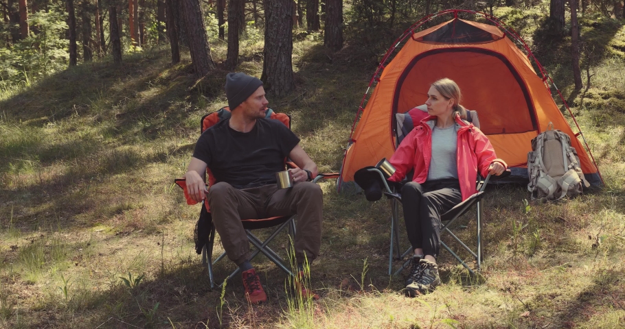 forest camping - young hiker couple enjoying cup of tee at campsite
