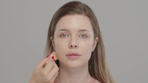 Makeup artist or stylist applies foundation using wet sponge to the face of the female model. Visagiste  applying cosmetic concealer base on a face. Professional makeup. Tutorial makeup master class  
