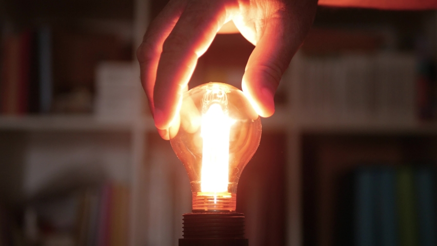A Hand Turning On a Light in the Room, Screwing in a Socket One Incandescent Light Bulb with Warm Light. | Shutterstock HD Video #1073419649