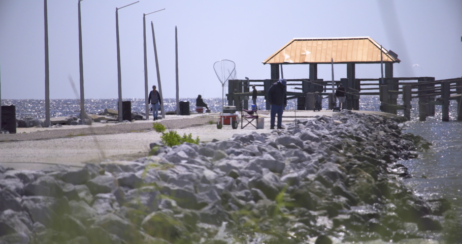 A diverse group of people fish on the foot of a broken pier. A scenic and serene setting in Coastal Mississippi (Gulfport-Biloxi) as people go fishing in the Gulf of Mexico.