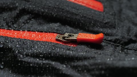 Water droplets on the waterproof fabric. Close-up of a waterproof jacket. Black clothes with red zipper