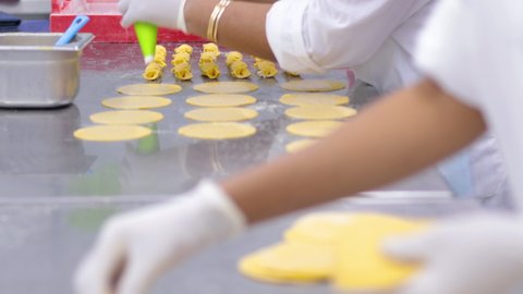 Woman with nylon gloves on, using a pastry bag to squeeze a cheese stuffing onto pasta circles, before folding them up.