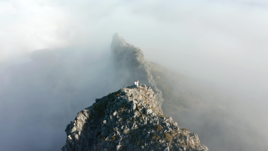 Adventure couple stands on steep rocky cliff above magical clouds in Madeira