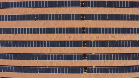 Top down ascending aerial view of solar panels in a large solar field in the desert