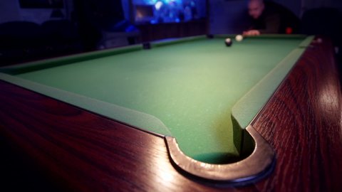 The eight ball is potted on a green pool table. The white ball is struck with a pool cue sending the 8-ball into the corner pocket.
