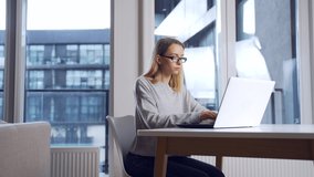 young female student working in the evening on a laptop at workplace herself. Woman freelancer alone in office or home typing front computer screen in modern room. Online learning or distance work