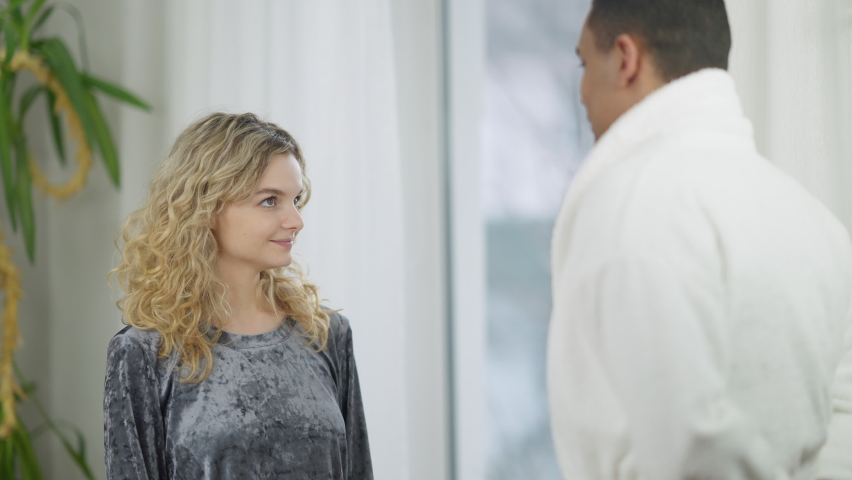 Portrait of young happy woman receiving bouquet of flowers in the morning and hugging loving man. Excited Caucasian girlfriend thanking African American boyfriend for surprise