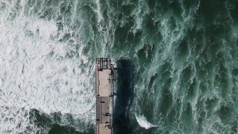 Rough ocean waves crashing under a council infrastructure project with tourist sightseeing. High drone view looking down