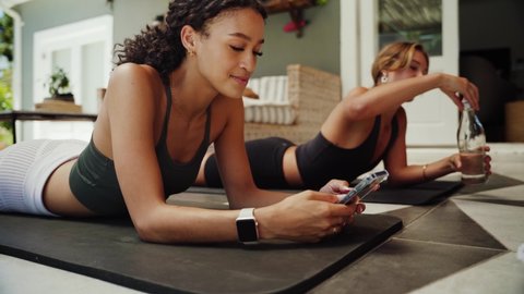Mixed race friends lying on gym mat scrolling on cellular device finding a good workout to do at home 