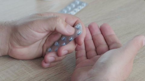 Close-up man's hands, pulls out pills with medicine from a blister pack to his palm, against the background of the table