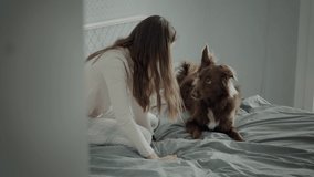 Mid shot of young cheerful girl lounging on bed with brown dog. A cinematic video card as a girl lies on a bed with a dog strokes and embraces it