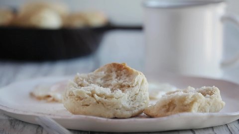 Woman's hand using a wooden spoon to pour hot steaming gravy over southern buttermilk biscuits. Selective focus with blurred foreground and background.