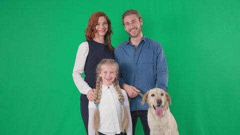 portrait of happy family of loving male and female parents with an adorable girl and labrador dog are smiling and looking at camera on green chrome key