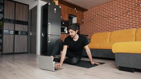 Fitness male athlete practicing online exercises on floor a mat using laptop at home in living room