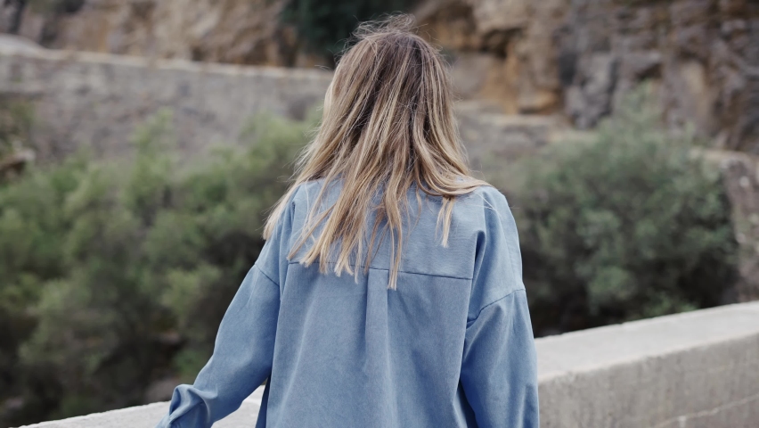 Woman tourist walks by the road bridge with view of the rocks and hills