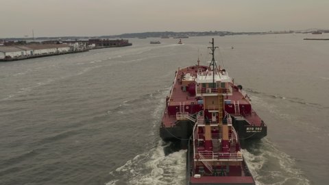 Close up aerial rotating view around a tugboat pushing a barge down the canal in container terminal of the New York City port, New York City, United States in 2019