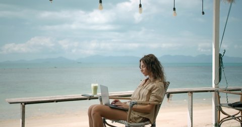 Woman seats at the beach bar alone and works as freelancer with laptop computer