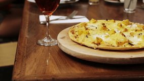Hawaiian pizza on wood board and glass of wine. Gourmet food concept, trucking left camera.