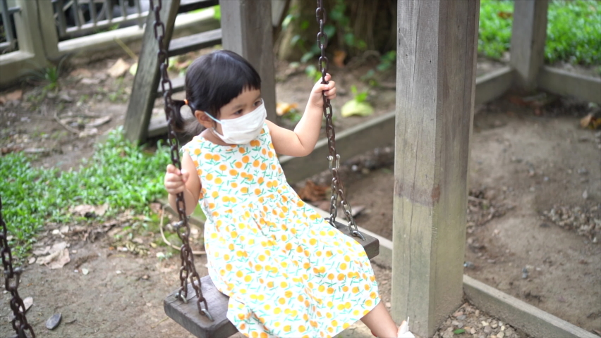 cute girl wearing surgical mask and playing with swing
