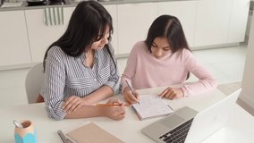 Young indian mum helping online virtual study to teen school girl at home sit at kitchen table using laptop. Mom with kid spending time teaching and learning, remote education with parent or tutor.