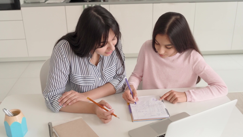 Young indian mum helping online virtual study to teen school girl at home sit at kitchen table using laptop. Mom with kid spending time teaching and learning, remote education with parent or tutor. Royalty-Free Stock Footage #1073447183