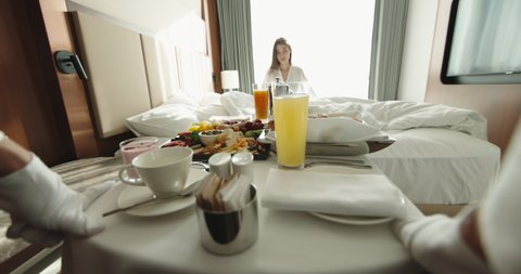 Waiter bringing cart with luxury breakfast into hotel room for customer early in morning. Hotel catering service setting meal 4k footage