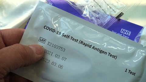London, UK, June 1st 2021: Covid-19 rapid self test kit, provided by the NHS for free. Holding a rapid antigen test package and then showing the step by step instruction guide for use. Flat lay static