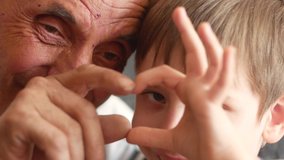 The grandson and grandfather show a heart gesture with the help of their hands. Cheerful Caucasian grandfather with a boy communicate and convey their love with a gesture. selective focus,  - Powered by Shutterstock - Get 15% off with code: PIKWIZARD15