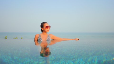 A young attractive woman leans against the edge of an infinity pool giving the illusion that she is floating on an ocean horizon.title space