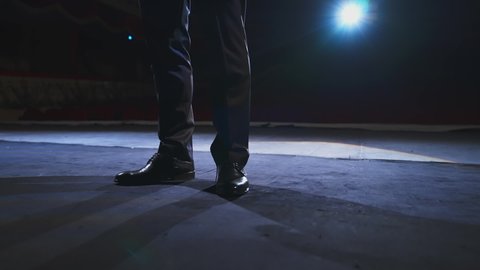 Actor's legs dancing on stage. Man in black shoes dancing against the theatre hall at dark scenic light. Close-up.