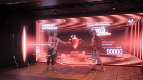 MOSCOW, RUSSIA - JANUARY 5, 2020: Technology AR exhibition. Two women posing with 3D big hologram projection in dark room. Future, augmented reality, immersive, entertainment, sci-fi concept