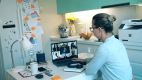 A worker in headset talks to people via laptop while staying home during pandemic. Videocall , video conference, online meeting, working remotely concept.