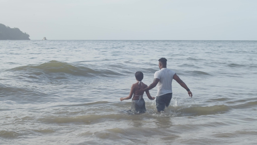 A couple walks into the ocean before diving into a wave