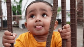 A child is trying to stand up holding a rusty iron rod in his small two hands. A kid is having fun and sticking out his tongue. Slow Motion video. 
