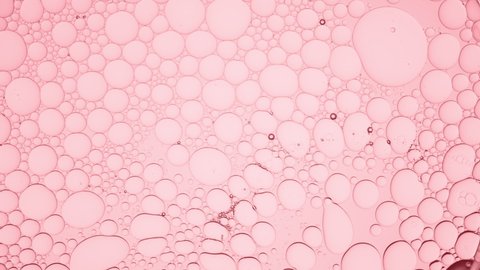 Big clear bubble slides along pale pink smaller ones moving them against pink background  Macro shot of emollient ingredients for its commercial