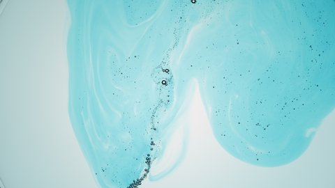 Cyan liquid with tiny grey transparent bubbles is injected into transparent one against pale blue background  Shot of skincare balm with hyaluronic acid for its commercial