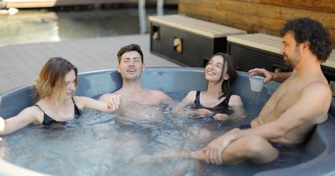 Company of friends bathing in outdoor hot vat at the luxury spa. Couples have fun and relax in wellness center