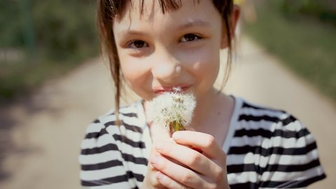 Portrait of a Happy Little Girl Blowing On A Dandelion And Smiling Close Up, overexposure