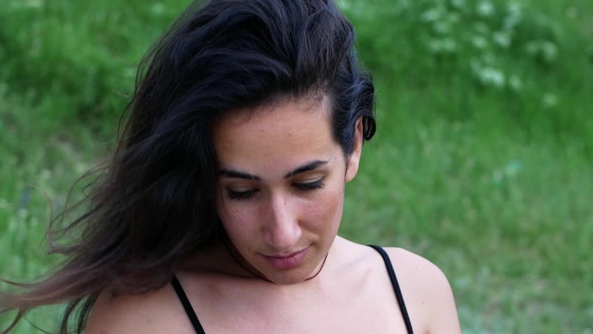 A beautiful young girl at sunset straightens her dark hair slowly fluttering in the wind with her hands.