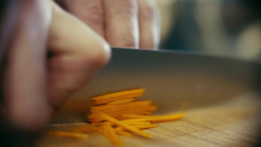 The chef cuts fresh carrots on a wooden board with a sharp knife. Macro shot.