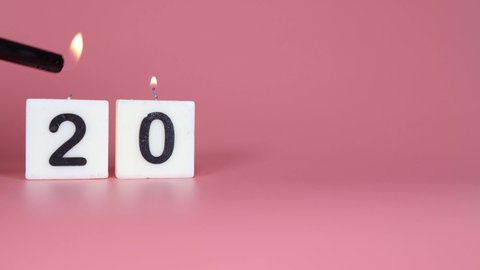 A square candle saying the number 20 being lit and blown out on a pink background celebrating a birthday or anniversary 