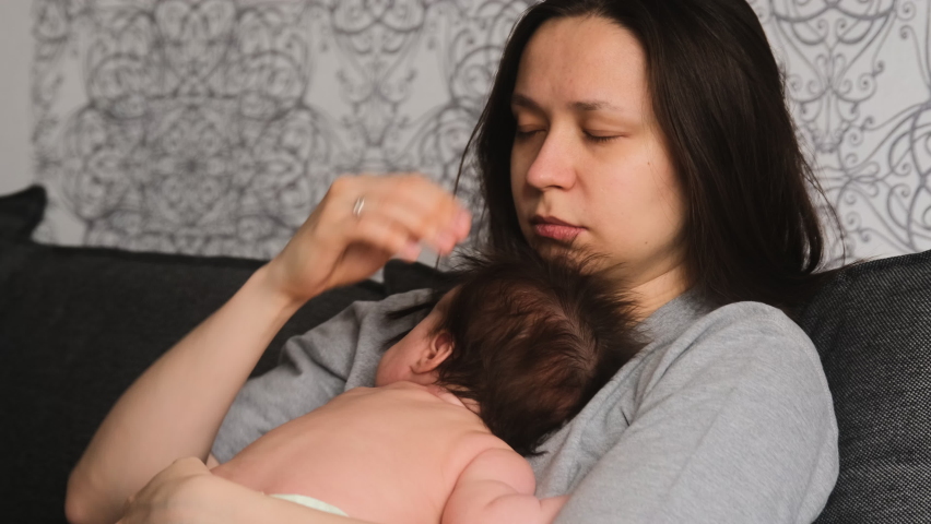 Authentic candid real life tired mother yawning while holding new born baby infant wants sleep and rest, sitting on bed at home.  Motherhood and child care. Royalty-Free Stock Footage #1073503190