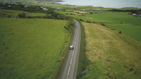 Ireland car riding road aerial view: rural green pasture and meadows in Irish. Coastline on horizon with ocean bay. Picturesque landscape of farmland in summer day. Footage shot in FullHD